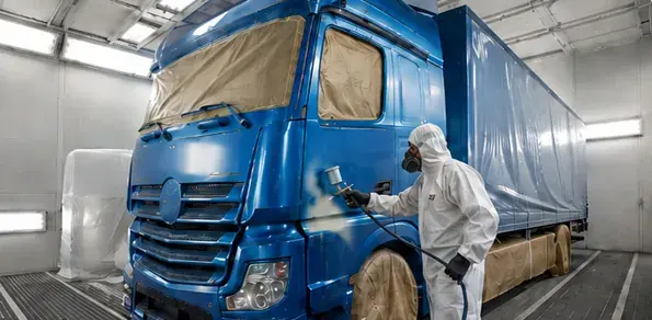 Blue commercial truck being spray painted inside a spray booth